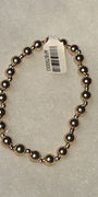 A beaded stretch bracelet made of polished metallic dark gold or rose-gold-toned beads, shown on a light gray textured background with a white product tag attached.