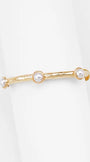 A gold-toned textured bangle bracelet with three white faux-pearl beads, displayed on a clean white background.