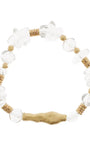 A beaded stretch bracelet featuring clear faceted crystal beads, small tan wooden beads, and a textured gold-toned central charm, displayed on a solid white background.
