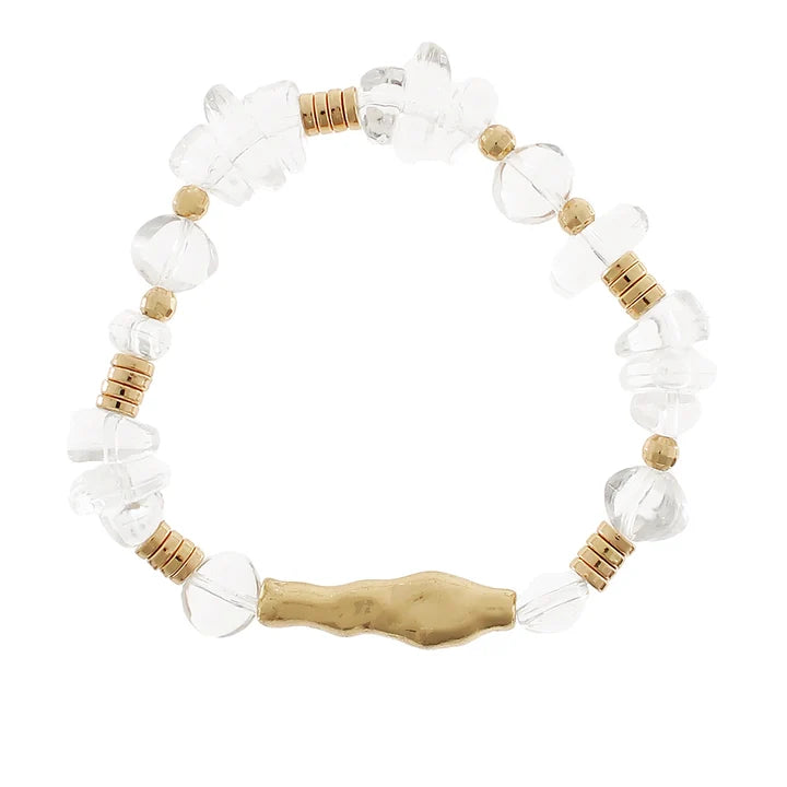 A beaded stretch bracelet featuring clear faceted crystal beads, small tan wooden beads, and a textured gold-toned central charm, displayed on a solid white background.
