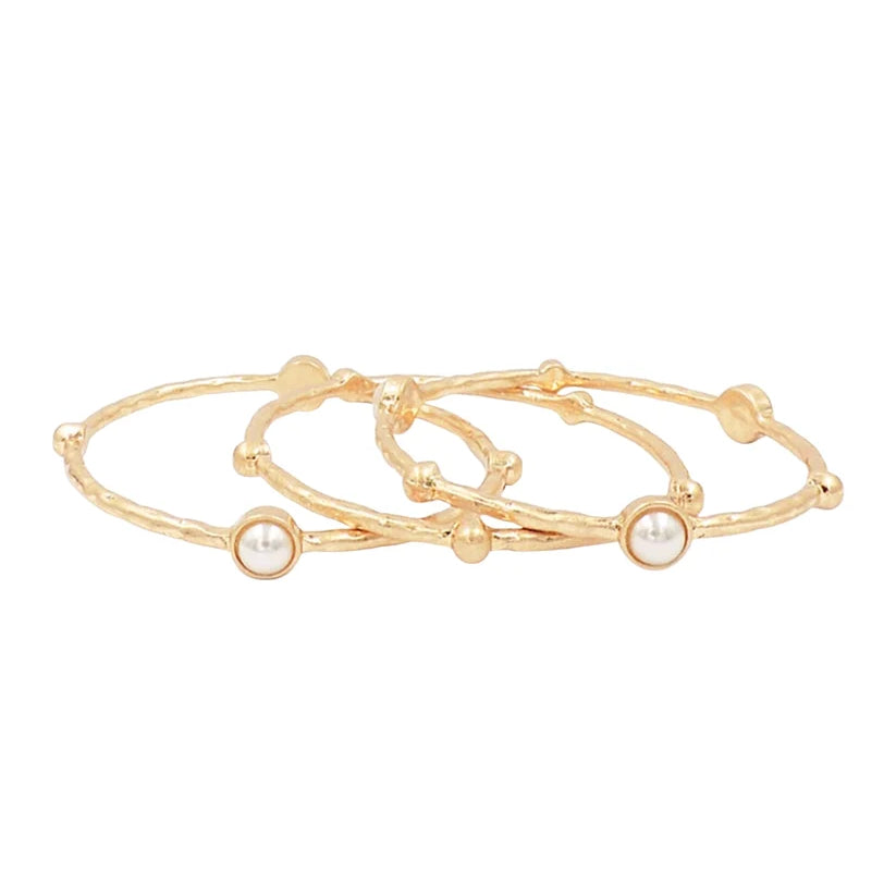 Three slim gold bangle bracelets with small bead details and round white pearl accents, arranged on a plain white background.