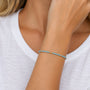 A delicate beaded bracelet with light blue beads and small gold spacer beads worn on a woman's wrist, shown against a white top.
