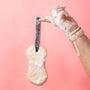 Hand holding a scrubber with soap suds against a pink background