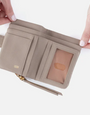 Beige wallet with a strap held open by hands on a white background