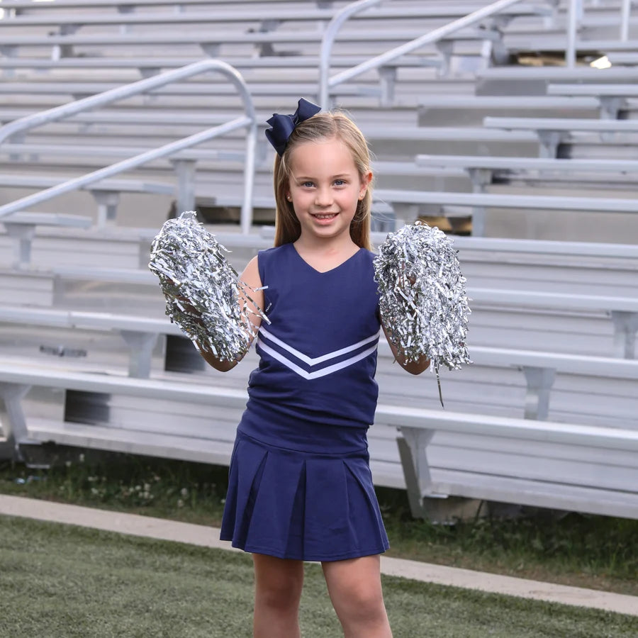 Young girl in a cheerleading outfit holding pom-poms in front of bleachers.