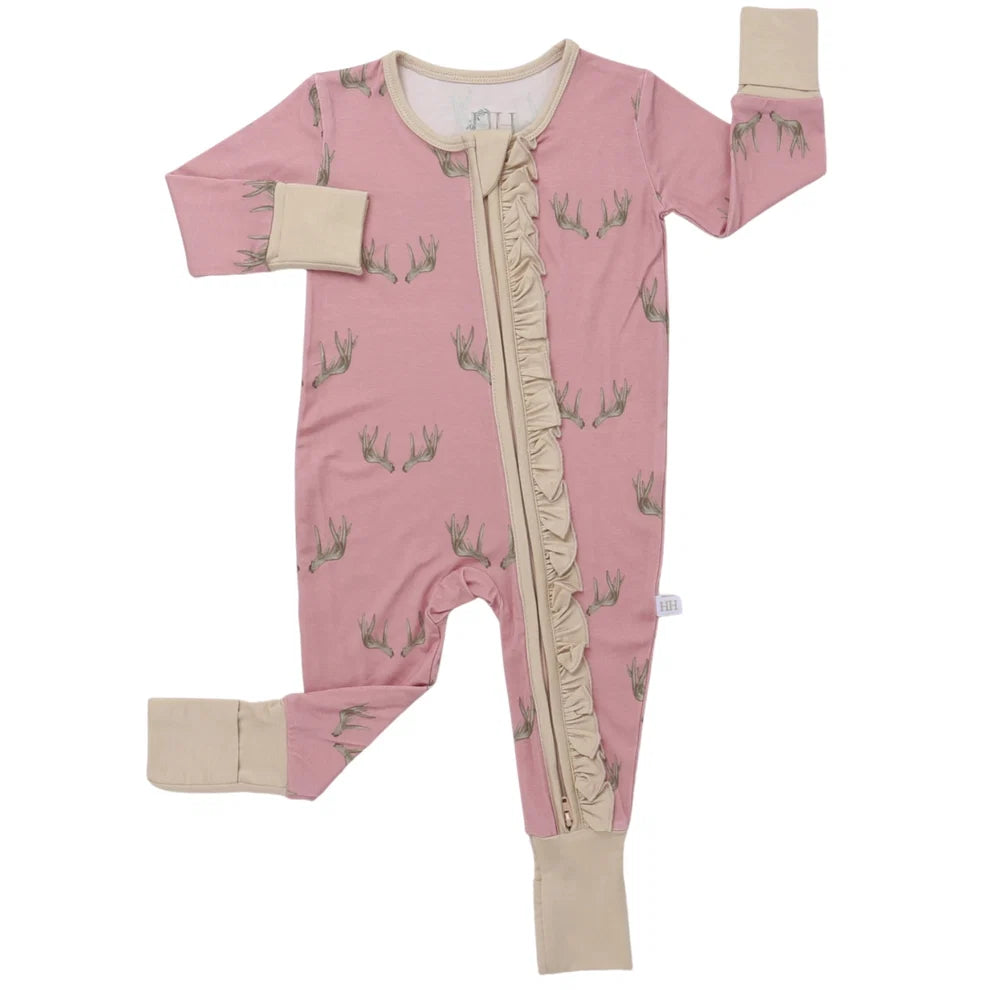 A baby's pink footed sleeper with a subtle pattern of small cartoon characters, featuring beige cuffs and a beige zipper closure down the front.