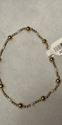 A beaded stretch bracelet with alternating metallic bronze and white beads, shown on a light gray textured background with a white product tag attached.