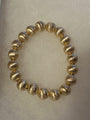 A beaded stretch bracelet made of metallic gold textured round beads, displayed on a light beige textured background.
