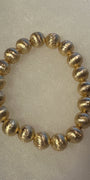 A beaded stretch bracelet made of metallic gold textured round beads, displayed on a light beige textured background.