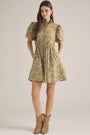 A woman modeling a short puff-sleeve dress with a beige and brown floral pattern, standing against a plain light beige studio background.