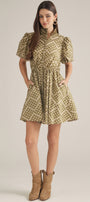 A woman modeling a short puff-sleeve dress with a beige and brown floral pattern, standing against a plain light beige studio background.