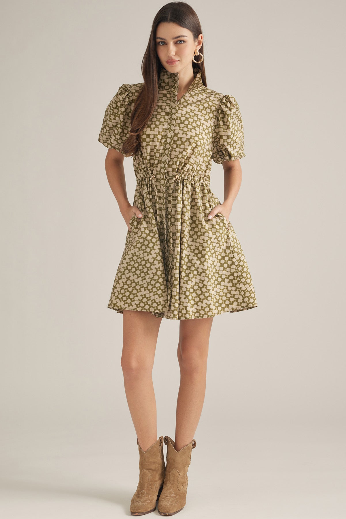 A woman modeling a short puff-sleeve dress with a beige and brown floral pattern, standing against a plain light beige studio background.