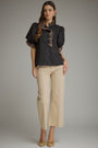 A woman modeling a black puff-sleeve blouse with leopard-print trim and buttons, paired with beige cropped trousers and beige pointed flats, against a plain gray studio background.