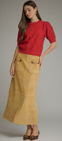 A woman modeling a red short-sleeve textured knit top paired with a mustard yellow suede skirt with front patch pockets, set against a plain gray studio background.