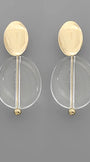 A pair of modern gold and clear acrylic drop earrings on a solid gray background.