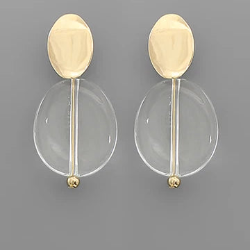 A pair of modern gold and clear acrylic drop earrings on a solid gray background.