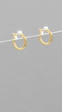 A pair of small gold hoop earrings with white gemstone accents, suspended on a thin white wire against a solid gray background.