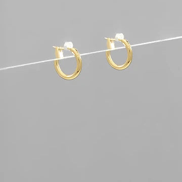 A pair of small gold hoop earrings with white gemstone accents, suspended on a thin white wire against a solid gray background.