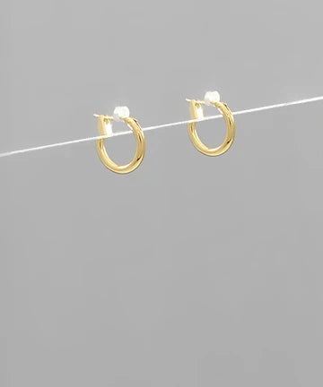 A pair of small gold hoop earrings with white gemstone accents, suspended on a thin white wire against a solid gray background.