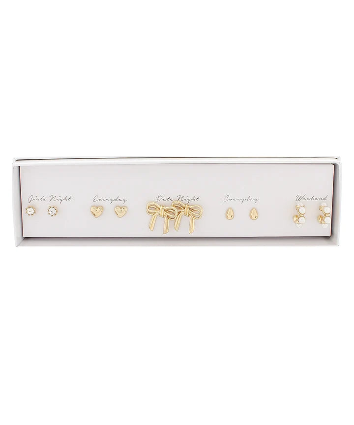 A set of five gold-toned stud earrings displayed in a white rectangular presentation box against a white background. The earrings include different designs such as a heart, a bow, teardrop, and floral motifs, with some labeled with handwritten text like 'Girls Night' and 'Everyday'.