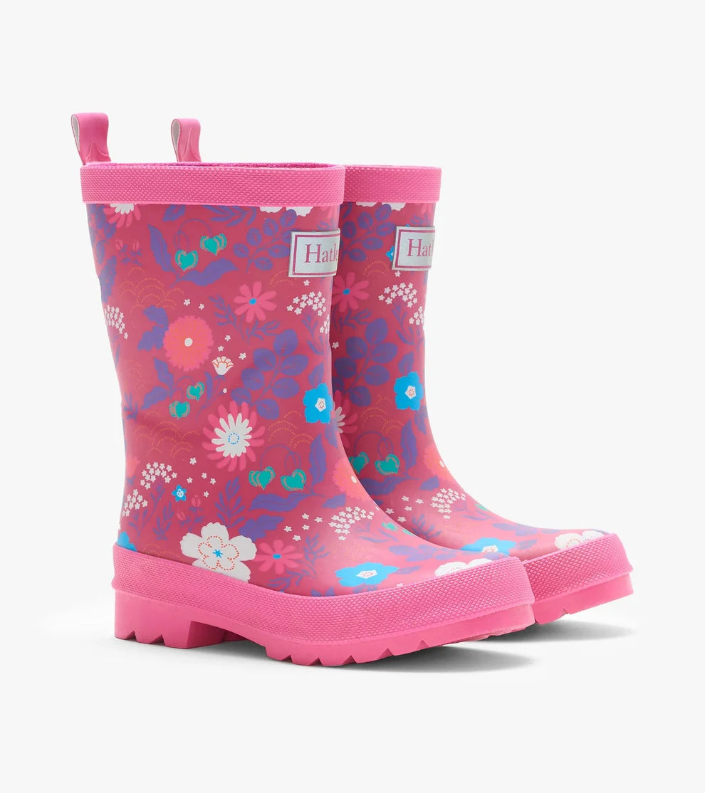 A pair of children's pink rubber rain boots with a colorful floral and abstract pattern, featuring pull tabs and a thick lug sole, shown on a light gray background.