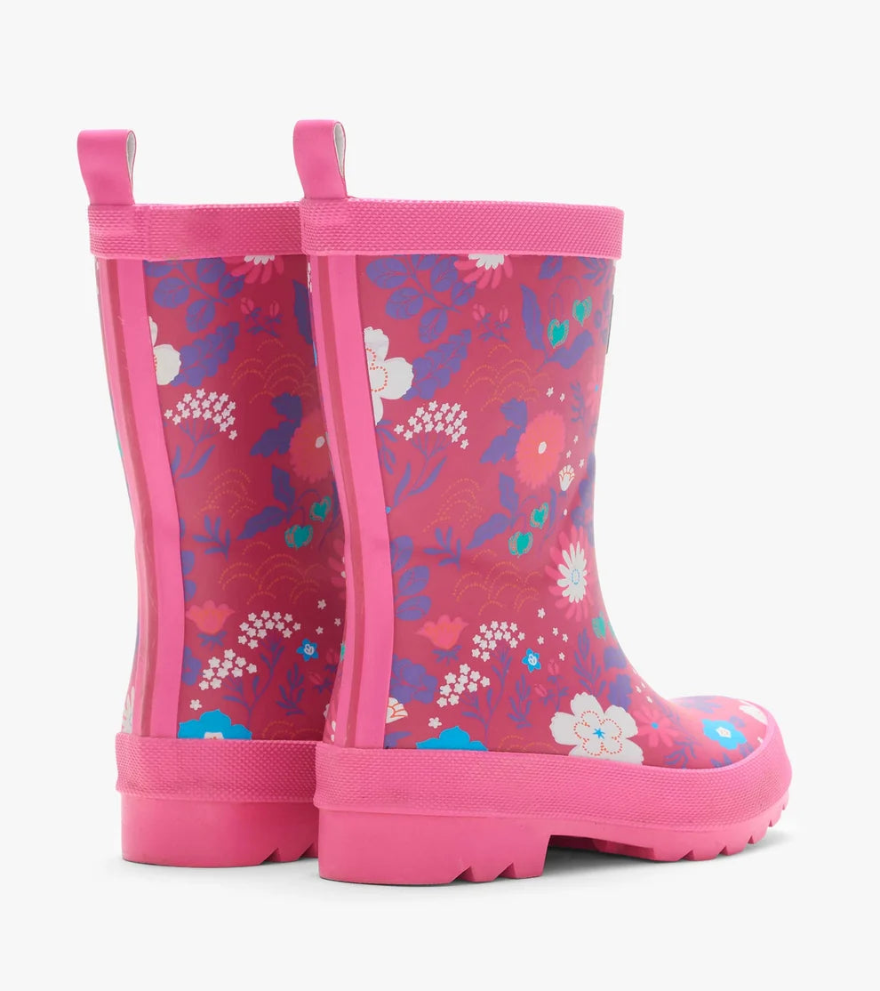 A pair of children's rain boots in vibrant pink, featuring a colorful floral and wave pattern on the upper and a solid pink sole and pull tabs, shown against a plain white background.