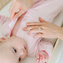 Baby in pink outfit with adult hands adjusting clothing