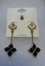 A pair of gold-tone dangle earrings with black enamel clover motifs, displayed on a white card backing labeled 'LEAD COMPLIANT'.