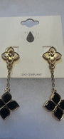 A pair of gold-tone dangle earrings with black enamel clover motifs, displayed on a white card backing labeled 'LEAD COMPLIANT'.