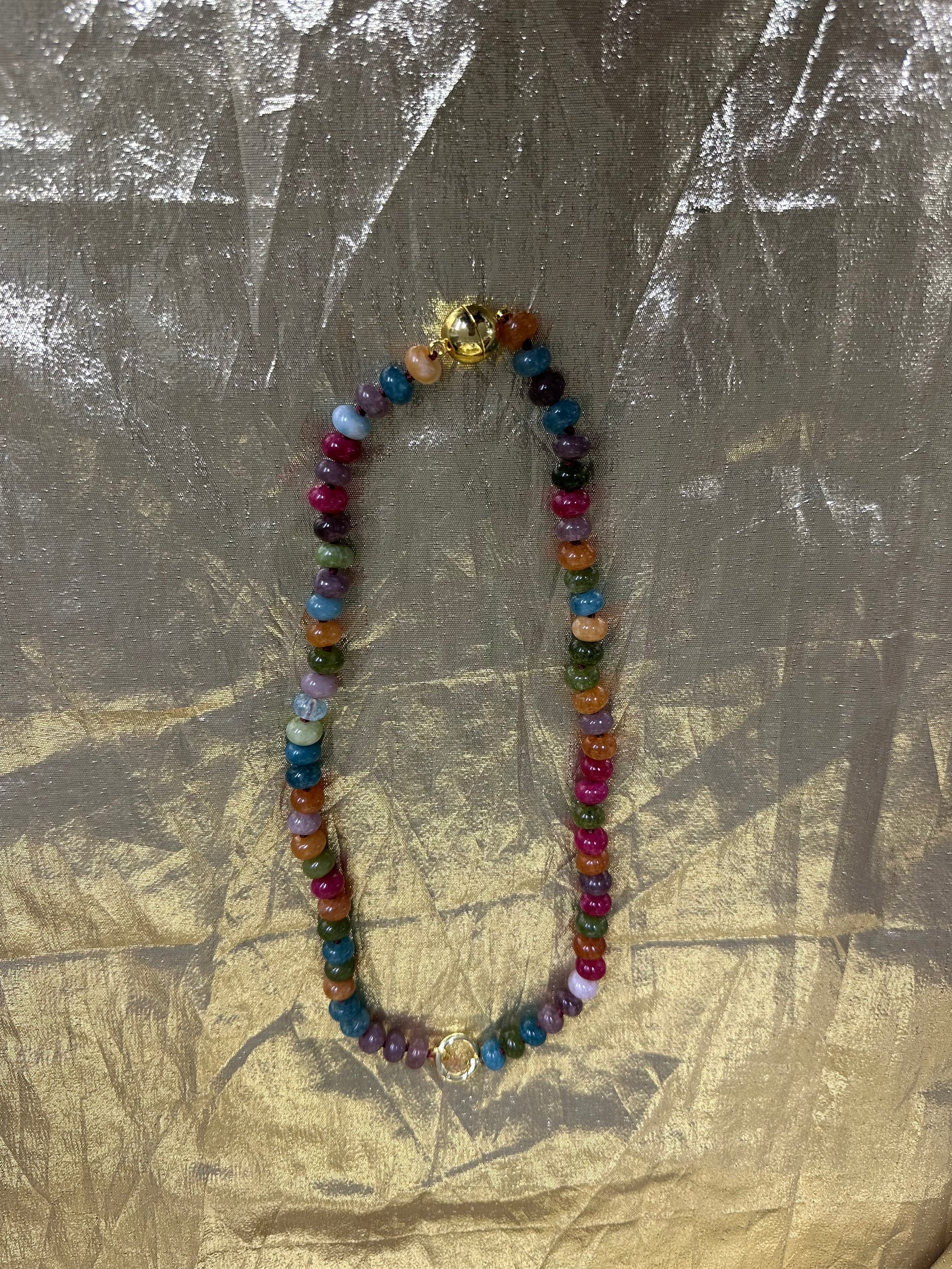 A multicolor beaded necklace with a gold clasp, laid flat on a textured gold foil background.