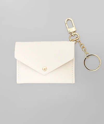 A small off-white envelope-style card holder or wallet with a gold snap button, attached to a gold keychain clip and ring, shown on a plain light gray background.