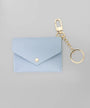 A light blue envelope-style card holder or coin purse with a gold snap button, attached to a gold keychain clasp and split ring, shown on a plain light gray background.