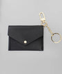 A black faux leather envelope-style card holder wallet with a gold-tone snap button, attached to a gold keychain clasp and split ring, shown on a neutral gray background.