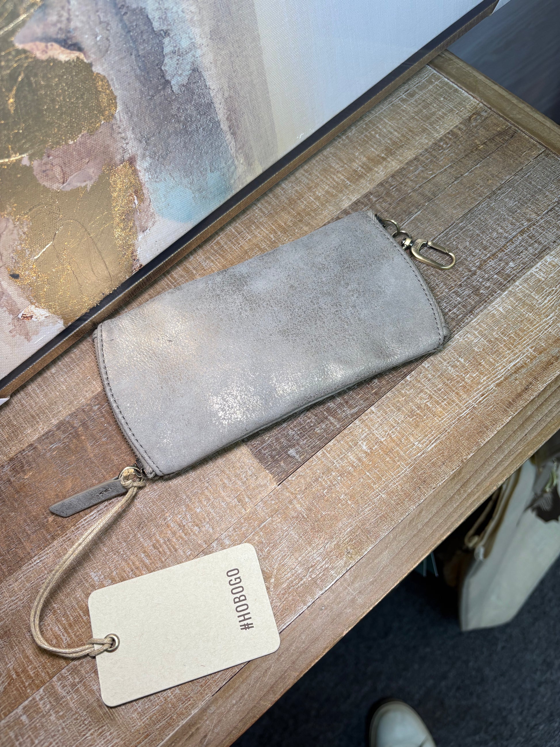 Gray suede pouch with a gold zipper on a wooden surface, accompanied by a beige tag.