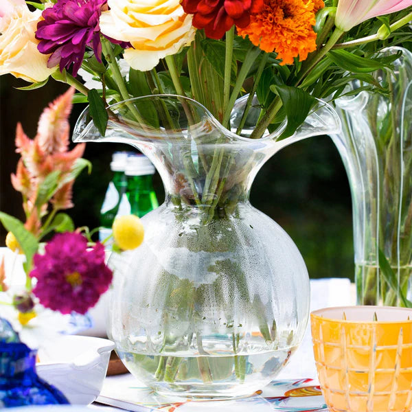 Clear glass pitcher with flowers on a table outdoors