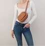 Person wearing a white long-sleeve top, blue jeans, and carrying a brown crossbody bag on a plain background