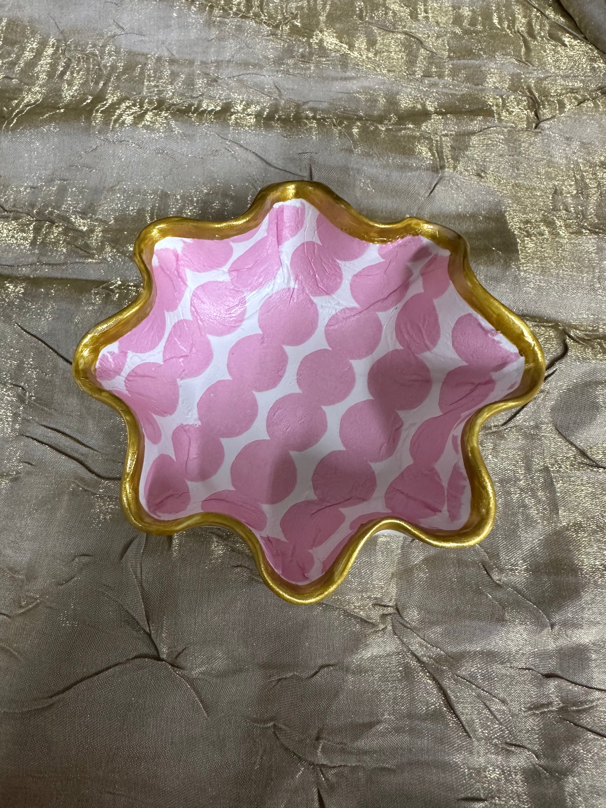 Decorative dish with pink and white pattern on a textured gold surface