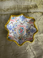 Decorative dish with floral pattern and gold rim on a textured gold surface