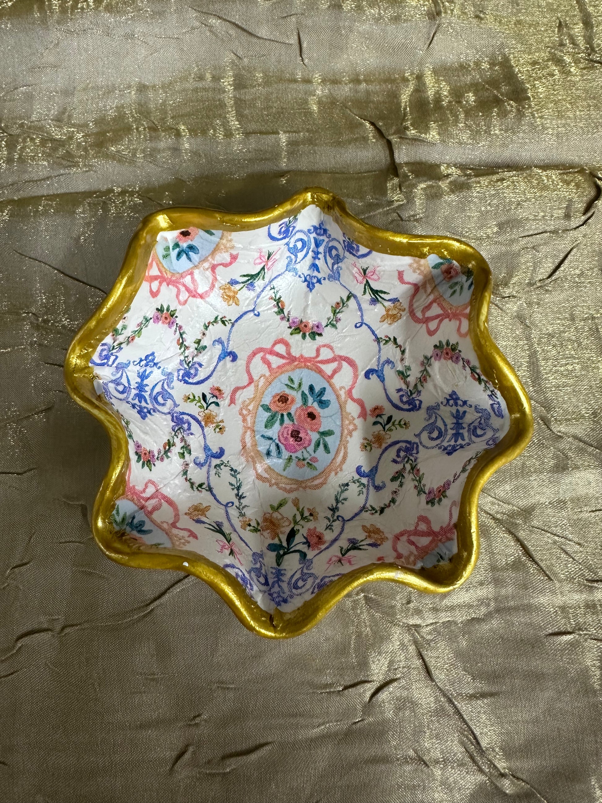 Decorative dish with floral pattern and gold rim on a textured gold surface