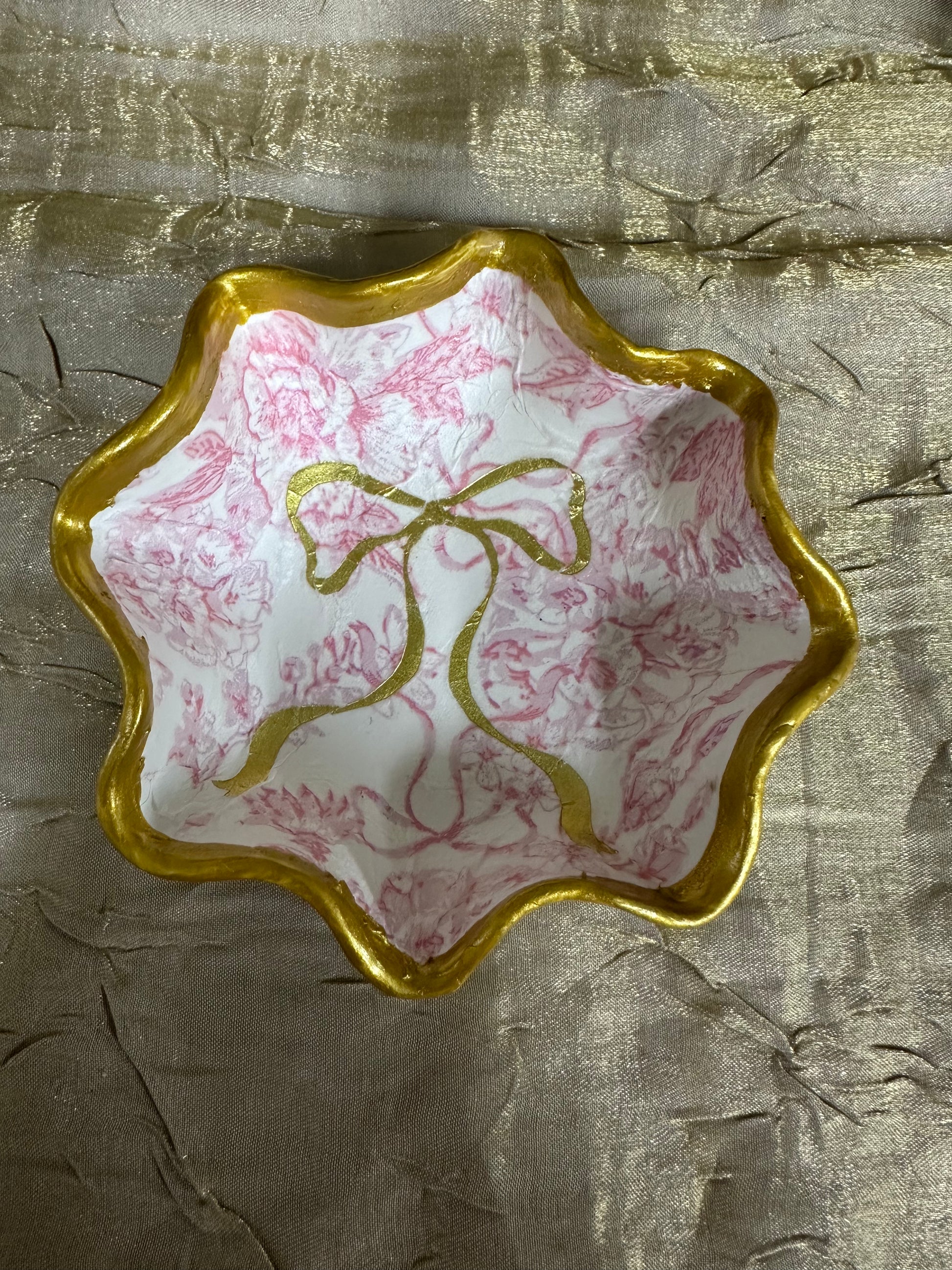 Decorative dish with gold rim and pink marbled design on a textured beige background