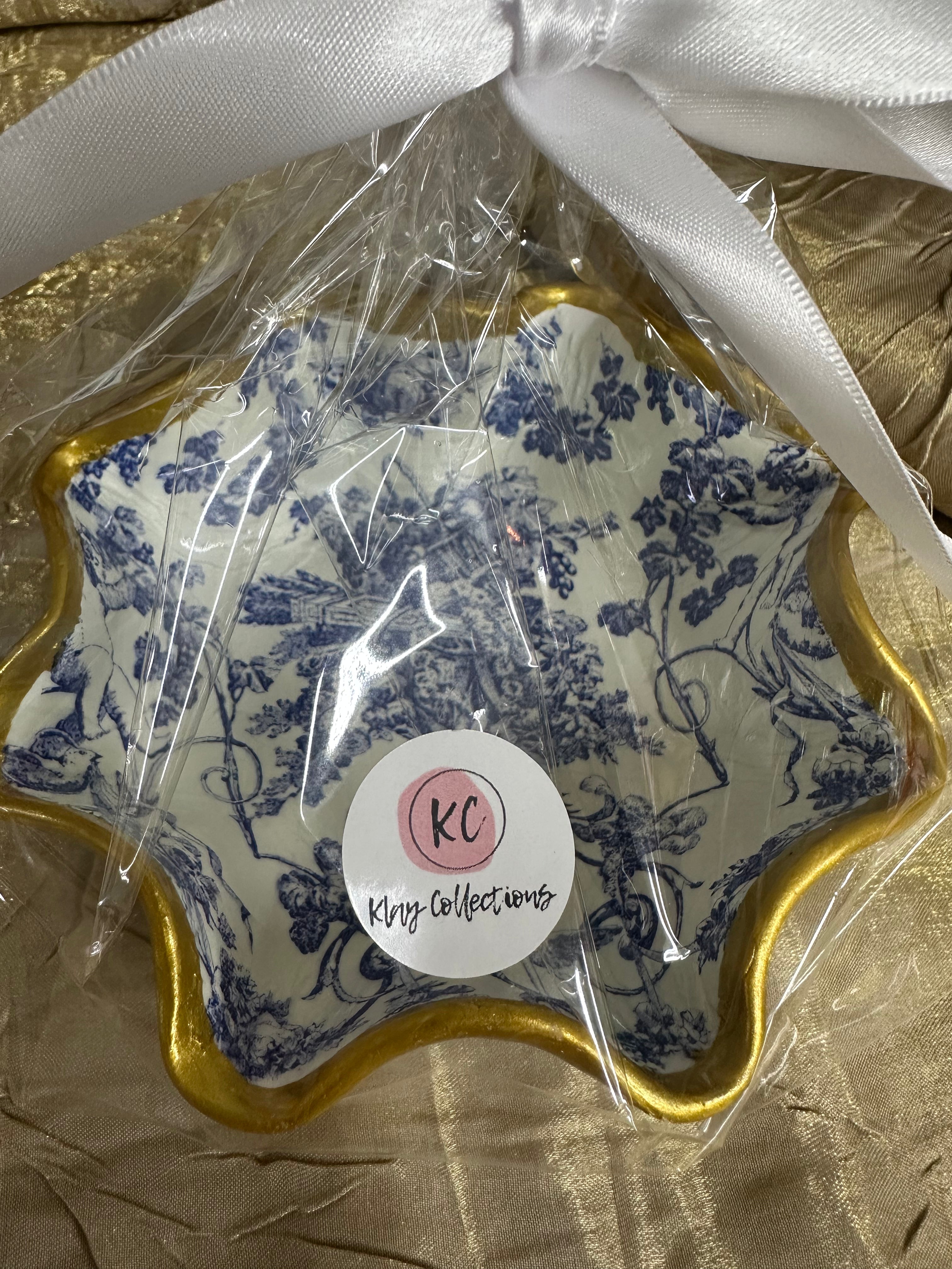 Decorative plate with blue floral pattern and gold rim, wrapped in clear plastic with a white ribbon on a brown surface.
