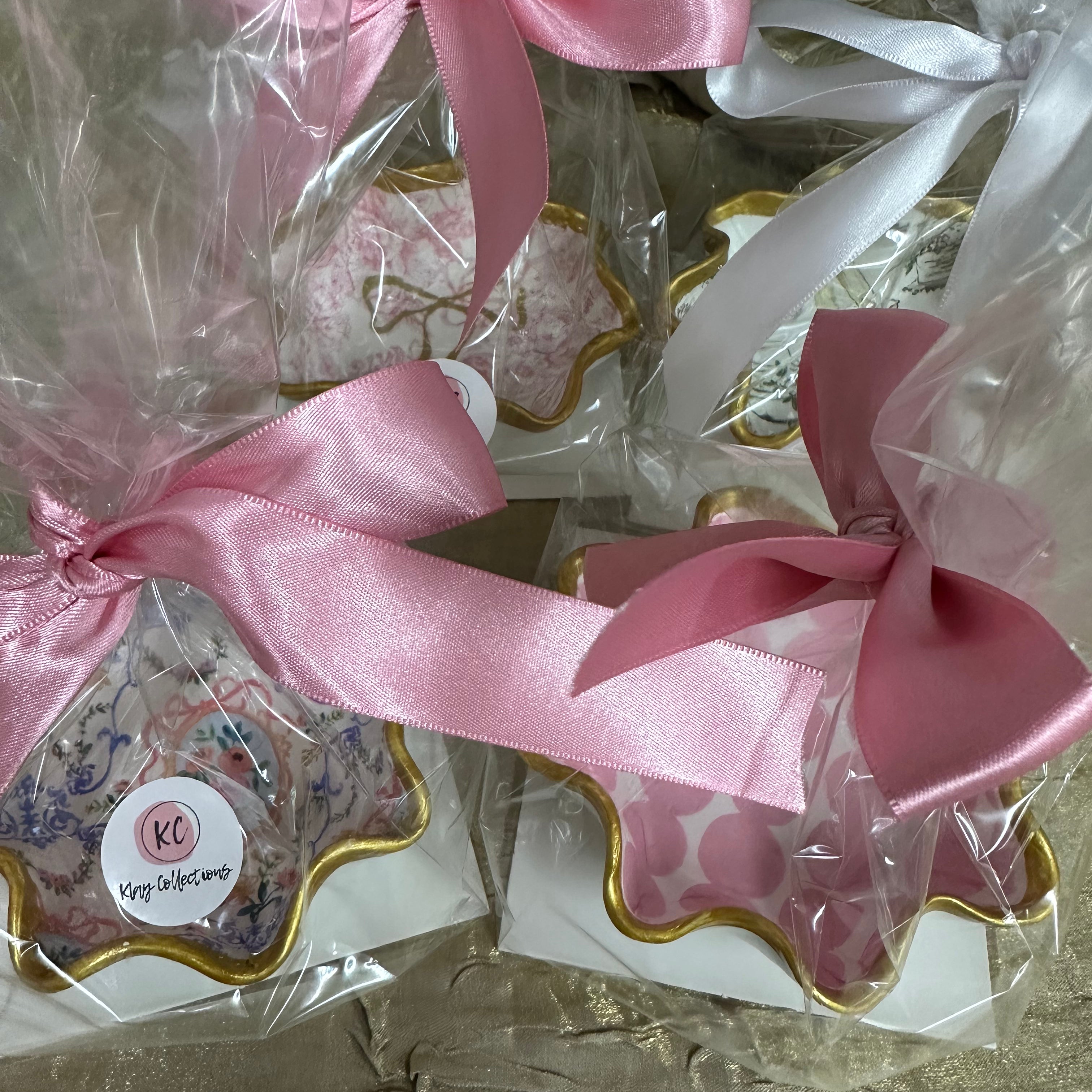 Decorative trinket dishes with pink ribbons and 'KC' branding on a textured surface.