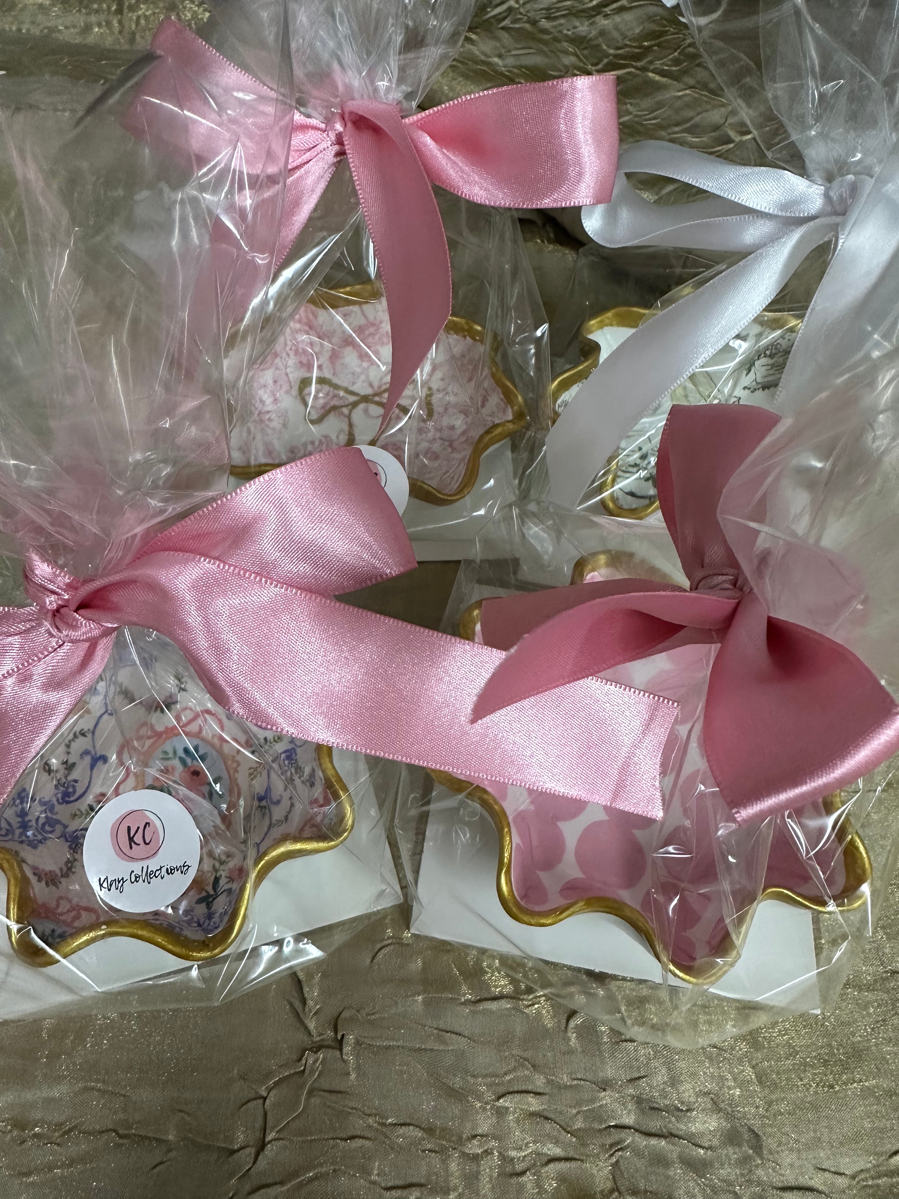 Decorative trinket dishes with pink ribbons and 'KC' branding on a textured surface.