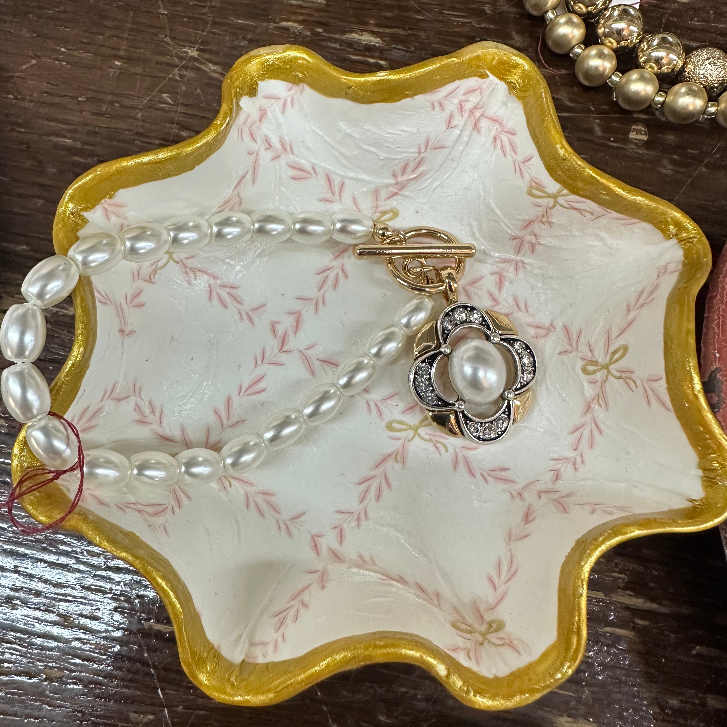 Jewelry dish with pearls and a ring on a wooden surface