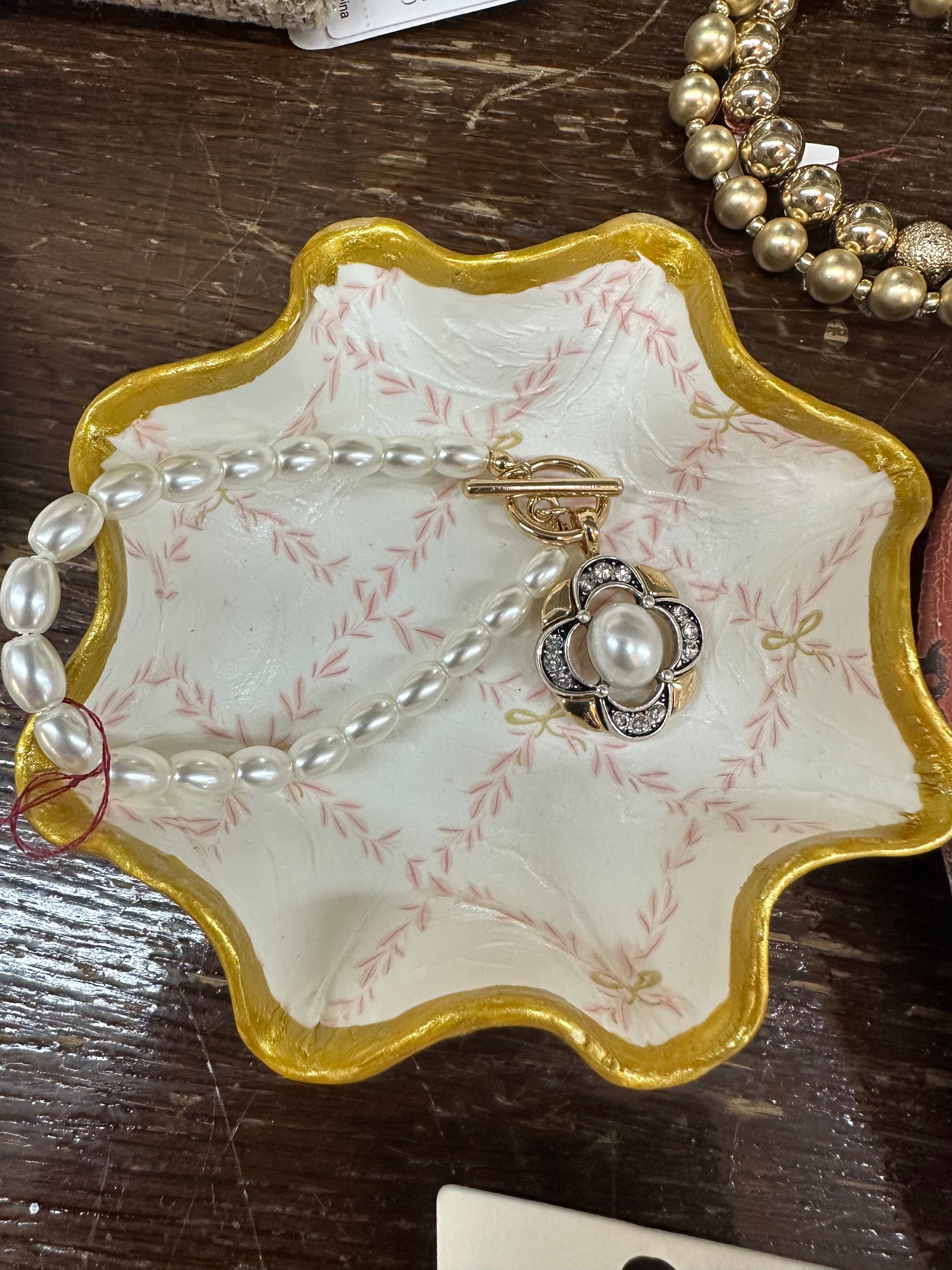 Jewelry dish with pearls and a ring on a wooden surface