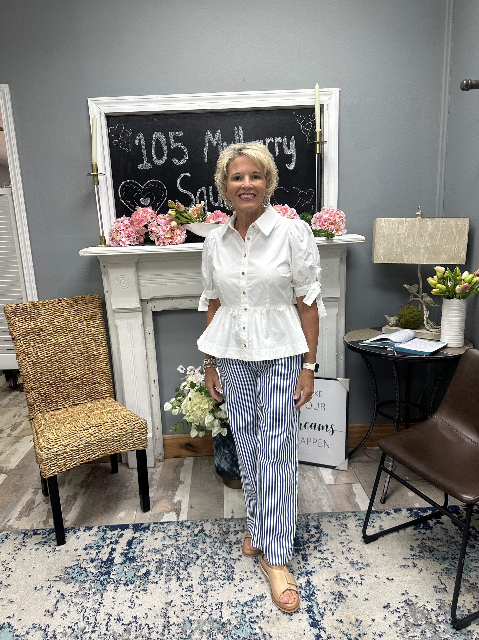 Woman standing in a room with a fireplace, chairs, and decorative elements.