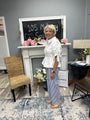 Woman standing in a room with decor elements like a fireplace, chair, and flowers.