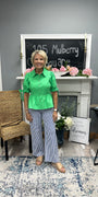 Woman in a green shirt and striped pants standing in a room with a chalkboard and decor.