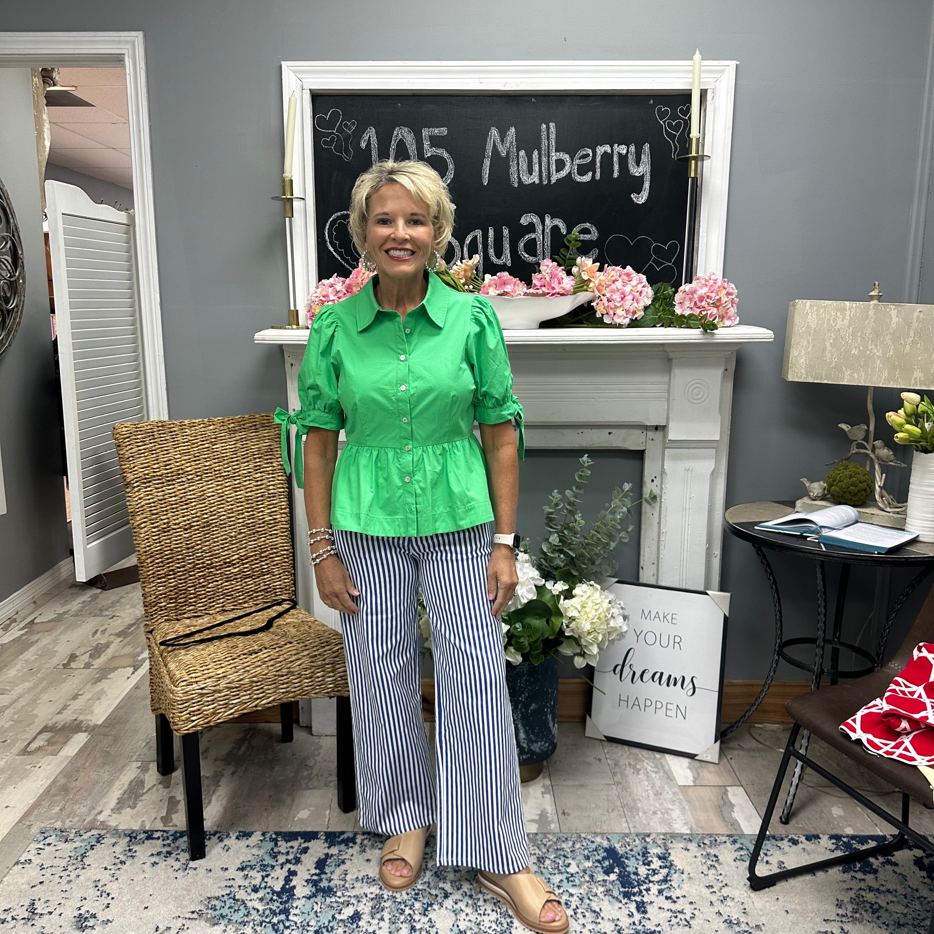 Woman in a green shirt and striped pants standing in a room with a chalkboard and decor.