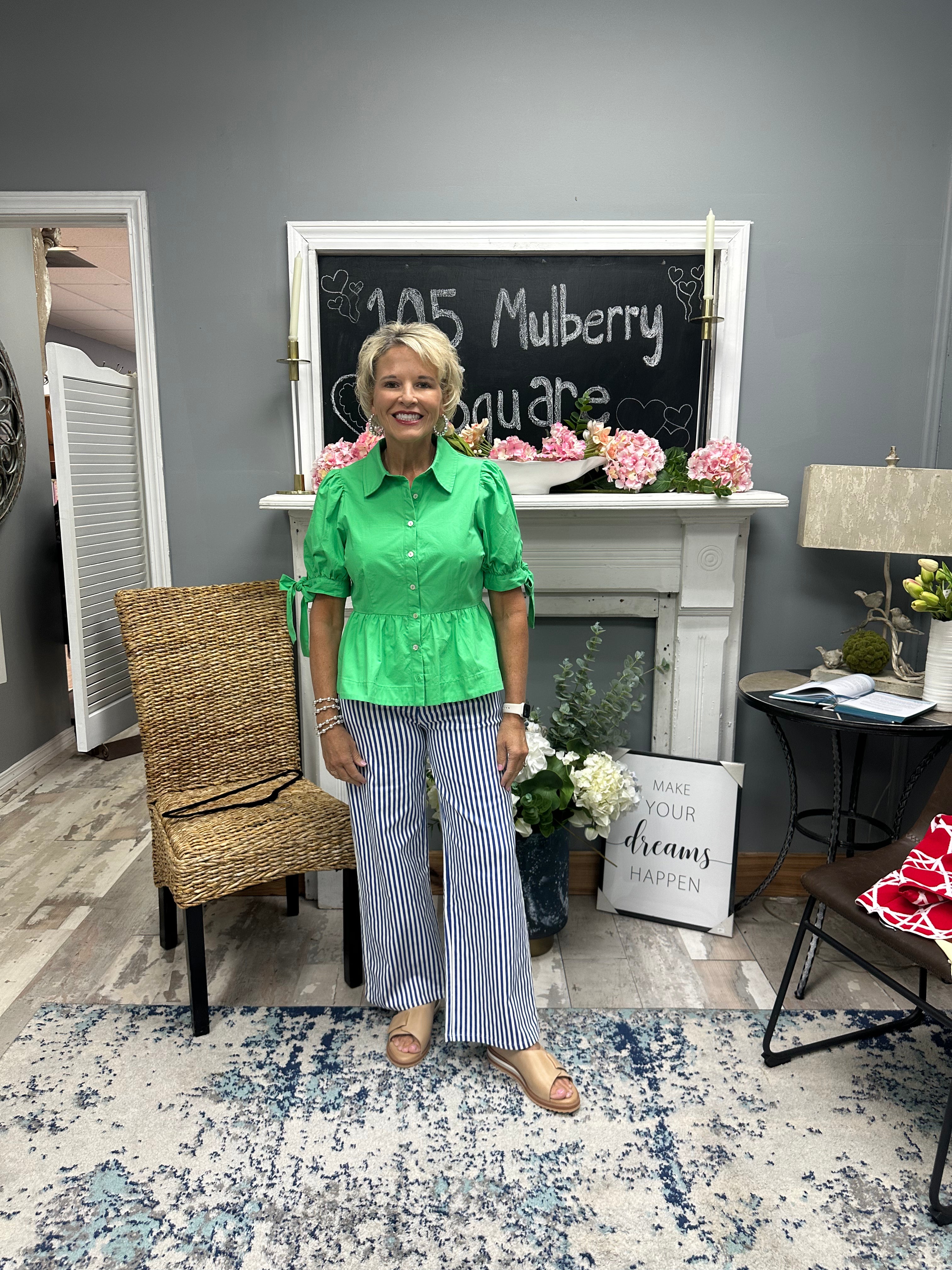 Woman in a green shirt and striped pants standing in a room with a chalkboard and decor.